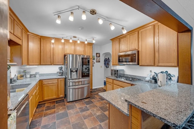 kitchen with sink, stainless steel appliances, kitchen peninsula, and light stone countertops