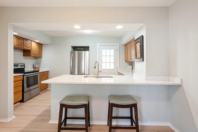 kitchen with a kitchen breakfast bar, appliances with stainless steel finishes, kitchen peninsula, sink, and light hardwood / wood-style flooring