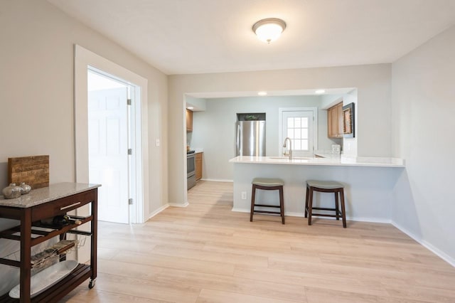 kitchen featuring sink, light hardwood / wood-style floors, kitchen peninsula, a breakfast bar, and appliances with stainless steel finishes