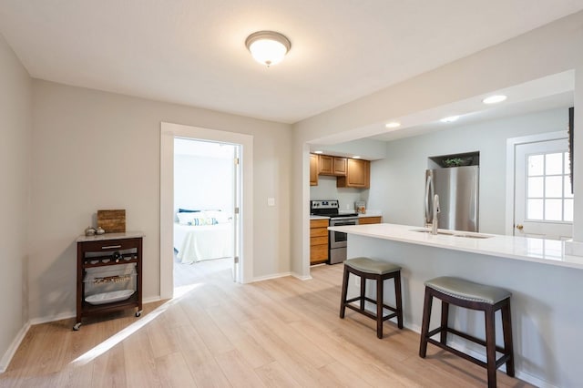 kitchen with kitchen peninsula, a kitchen bar, light wood-type flooring, appliances with stainless steel finishes, and sink