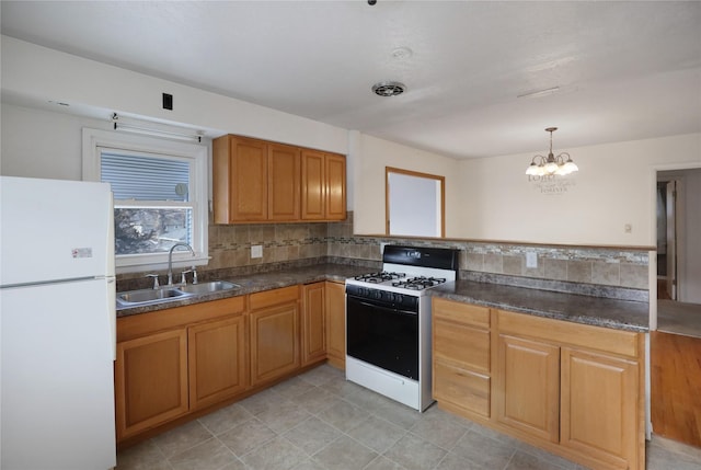 kitchen featuring white refrigerator, sink, an inviting chandelier, gas range oven, and pendant lighting