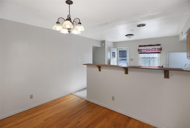 kitchen featuring white fridge, a breakfast bar area, kitchen peninsula, an inviting chandelier, and decorative light fixtures