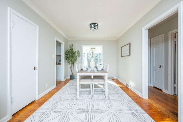 dining space with ornamental molding and light wood-type flooring