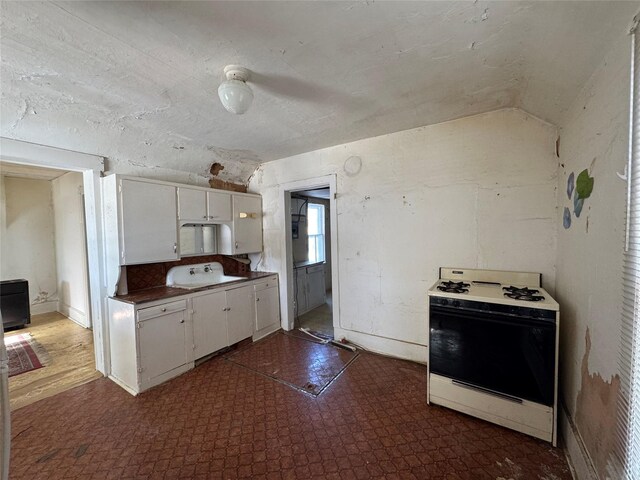 kitchen featuring lofted ceiling, white range with gas cooktop, and white cabinetry