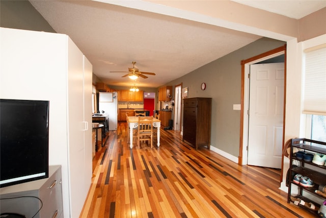 interior space featuring fridge, a breakfast bar, ceiling fan, and light hardwood / wood-style floors