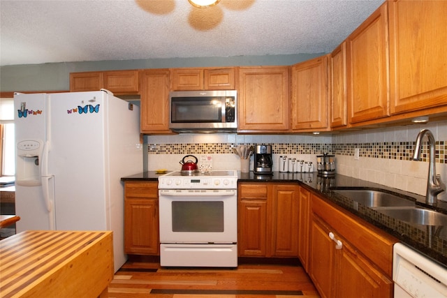 kitchen featuring white appliances, dark stone counters, a textured ceiling, sink, and backsplash