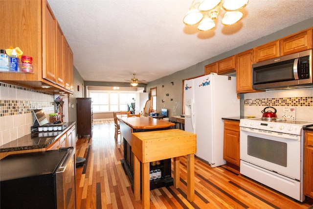 kitchen with white appliances, a textured ceiling, decorative backsplash, light wood-type flooring, and ceiling fan