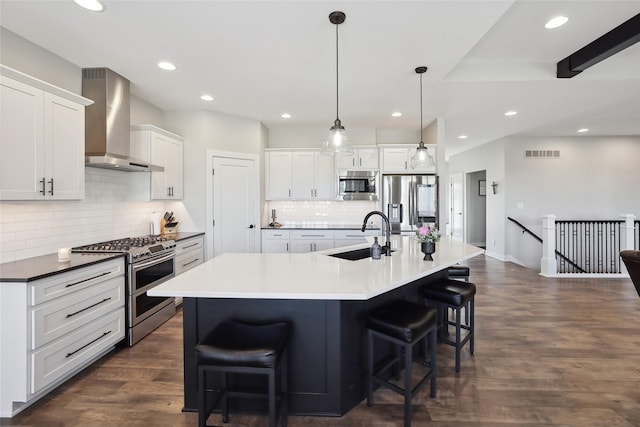 kitchen featuring hanging light fixtures, wall chimney range hood, white cabinets, appliances with stainless steel finishes, and sink