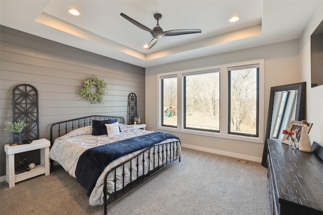 bedroom with wooden walls, a raised ceiling, ceiling fan, and carpet