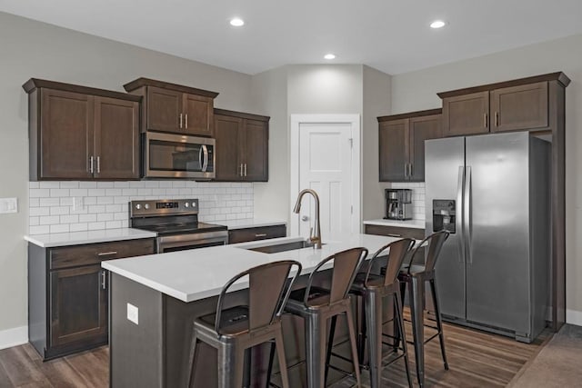 kitchen with a breakfast bar area, appliances with stainless steel finishes, an island with sink, dark hardwood / wood-style floors, and sink