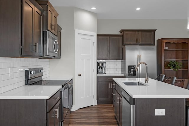 kitchen featuring a kitchen island with sink, appliances with stainless steel finishes, dark wood-type flooring, decorative backsplash, and sink