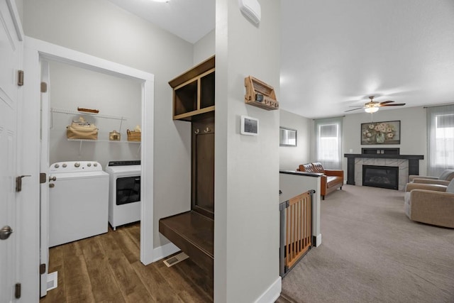 mudroom with washing machine and dryer, a tiled fireplace, ceiling fan, and dark hardwood / wood-style floors