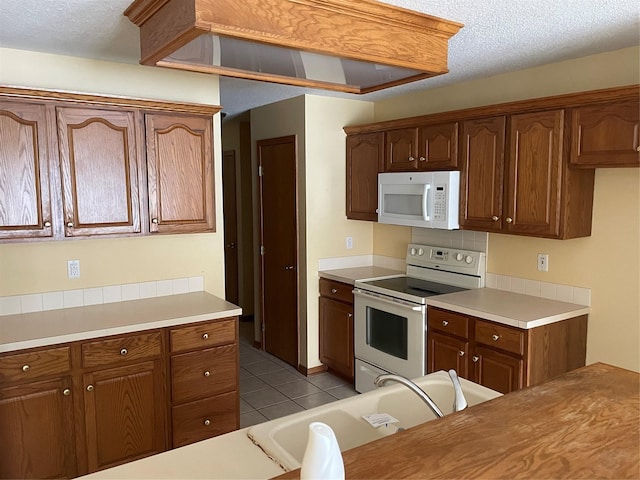 kitchen with sink, white appliances, a textured ceiling, and light tile patterned floors