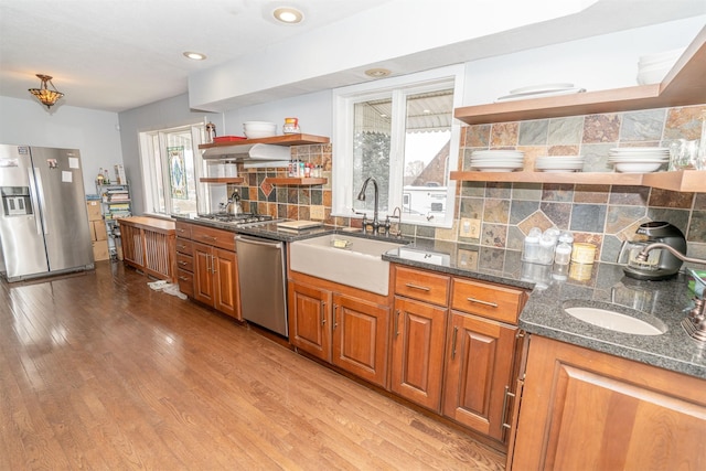 kitchen with light hardwood / wood-style floors, tasteful backsplash, dark stone counters, appliances with stainless steel finishes, and sink