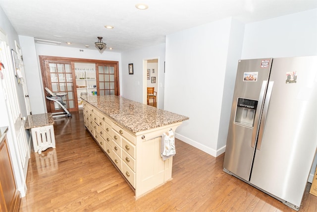 kitchen with a center island, cream cabinets, light hardwood / wood-style flooring, light stone countertops, and stainless steel refrigerator with ice dispenser