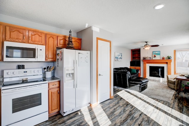 kitchen featuring white appliances, dark wood-type flooring, a textured ceiling, a tile fireplace, and ceiling fan