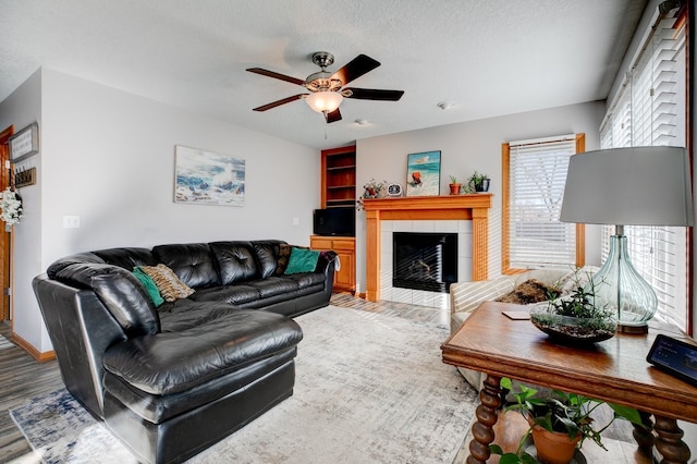 living room featuring wood-type flooring, a fireplace, ceiling fan, and a textured ceiling