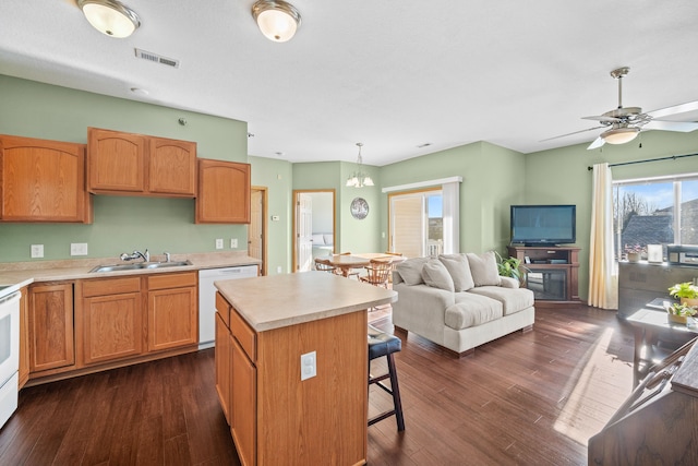 kitchen with white appliances, dark wood-type flooring, decorative light fixtures, a kitchen island, and sink