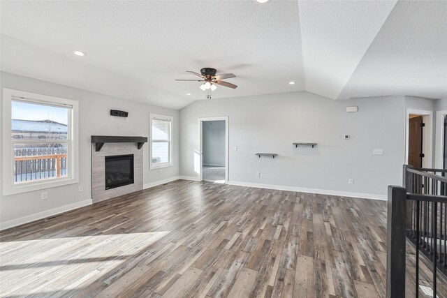 unfurnished living room with ceiling fan, a tile fireplace, vaulted ceiling, and hardwood / wood-style flooring