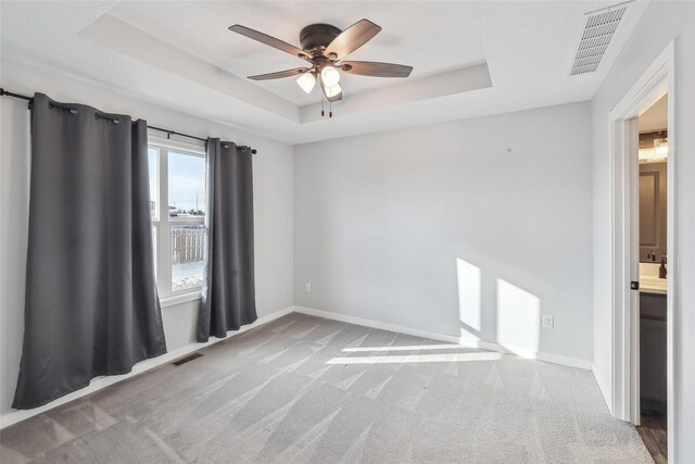 carpeted spare room featuring a raised ceiling and ceiling fan