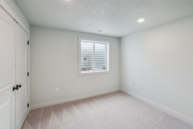 unfurnished bedroom with a textured ceiling, light colored carpet, and a closet