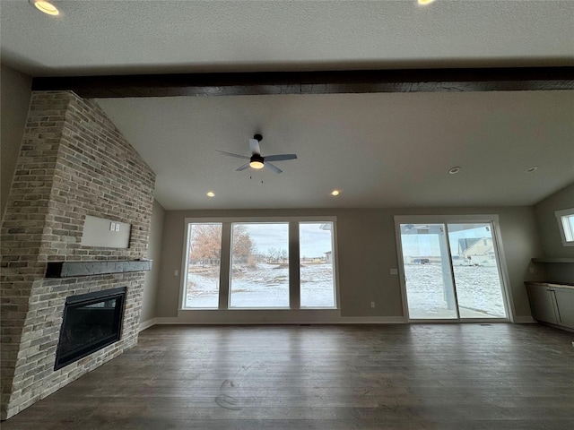 unfurnished living room featuring a fireplace, ceiling fan, a wealth of natural light, and vaulted ceiling with beams