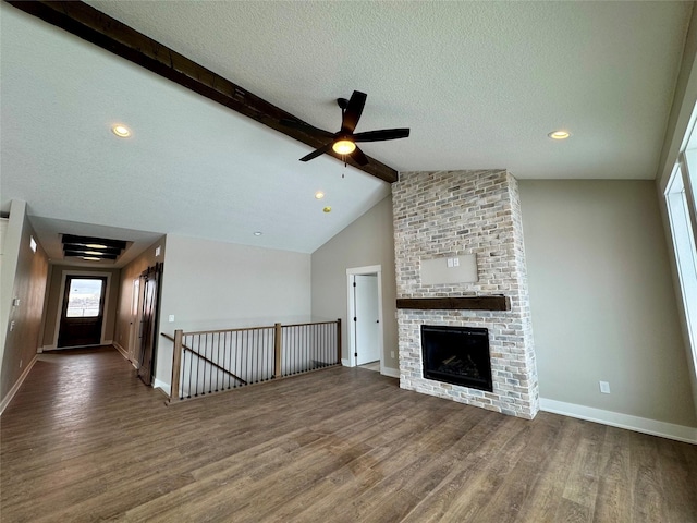 unfurnished living room with a textured ceiling, vaulted ceiling with beams, ceiling fan, a brick fireplace, and dark hardwood / wood-style floors