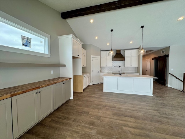 kitchen with a barn door, a center island with sink, hanging light fixtures, premium range hood, and sink