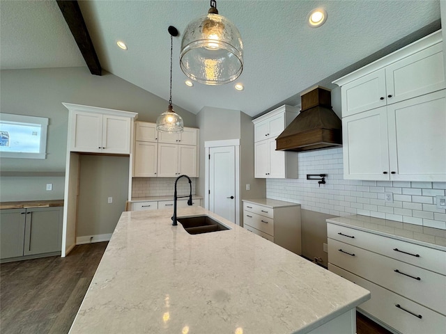 kitchen featuring light stone countertops, hanging light fixtures, tasteful backsplash, custom range hood, and sink