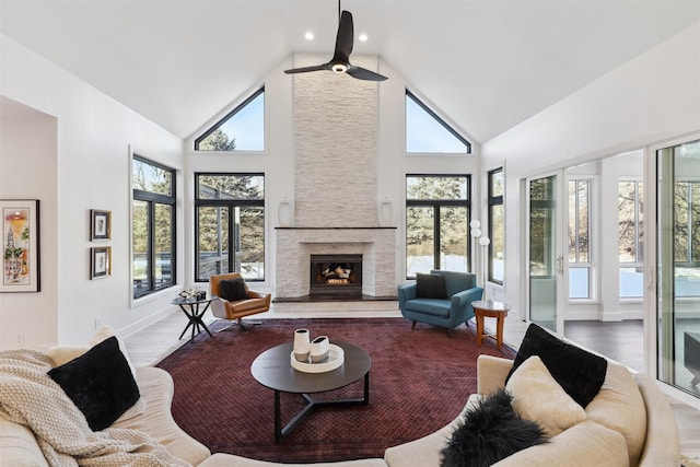 living room featuring high vaulted ceiling, ceiling fan, wood-type flooring, and a stone fireplace