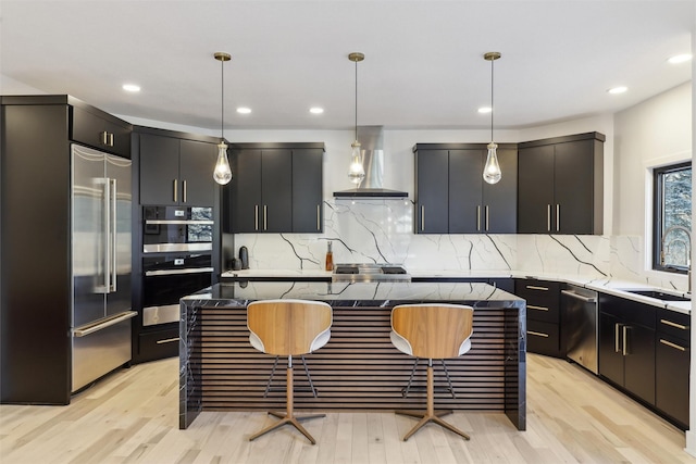 kitchen with stainless steel appliances, wall chimney range hood, hanging light fixtures, and a center island