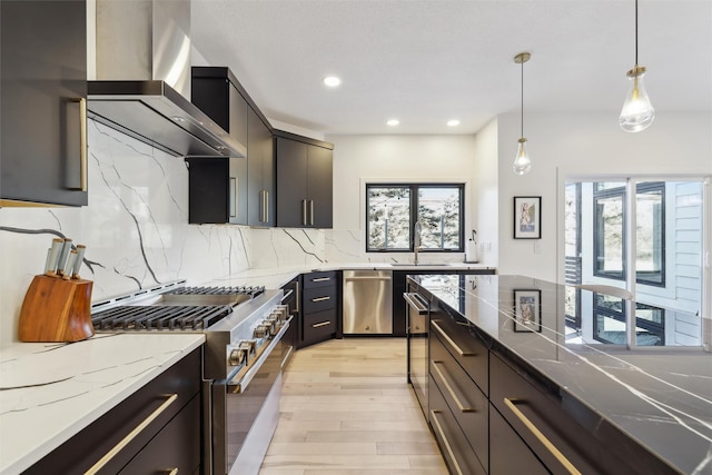 kitchen with stainless steel appliances, light wood-type flooring, decorative backsplash, hanging light fixtures, and wall chimney range hood