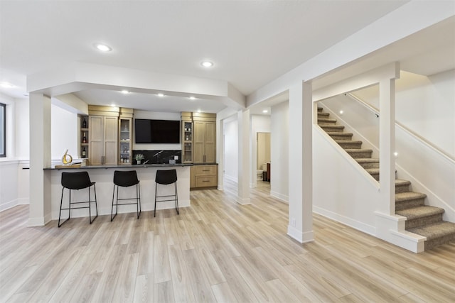 kitchen with kitchen peninsula, light hardwood / wood-style floors, backsplash, and a kitchen breakfast bar