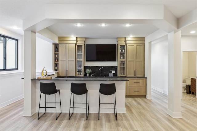 kitchen with kitchen peninsula, light hardwood / wood-style floors, tasteful backsplash, a breakfast bar area, and light brown cabinets