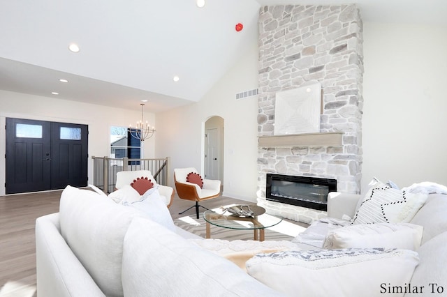 living room with light hardwood / wood-style flooring, a stone fireplace, high vaulted ceiling, and a chandelier