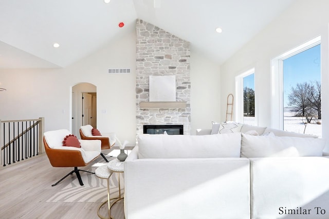 living room with light wood-type flooring, high vaulted ceiling, and a fireplace