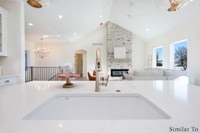 kitchen featuring light stone countertops, decorative light fixtures, high vaulted ceiling, a fireplace, and sink