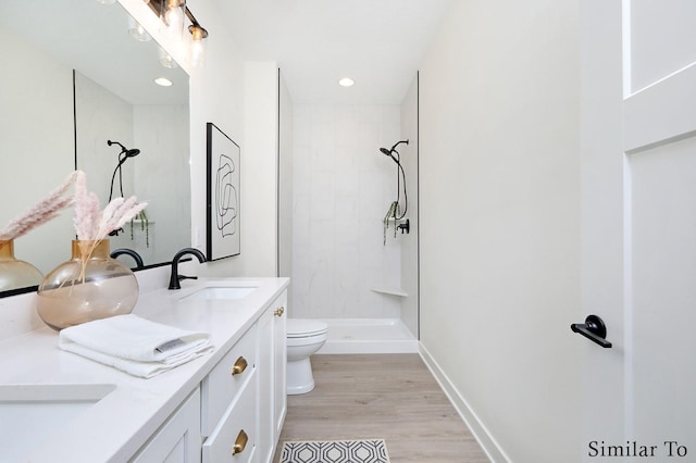 bathroom with hardwood / wood-style floors, a tile shower, vanity, and toilet