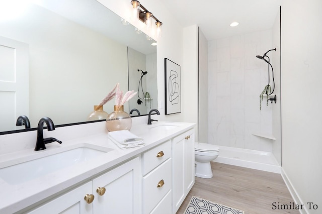 bathroom featuring toilet, wood-type flooring, tiled shower, and vanity