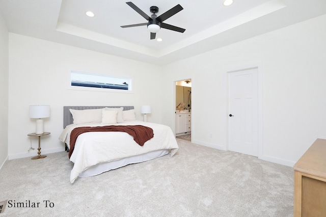 bedroom with ceiling fan, a tray ceiling, light carpet, and connected bathroom