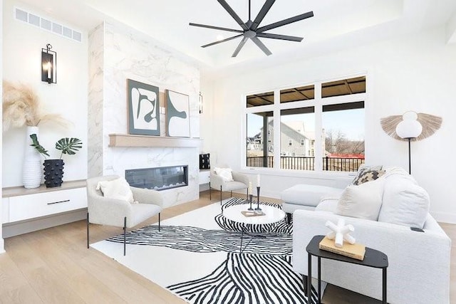 living area with light wood-style floors, a fireplace, visible vents, and a raised ceiling