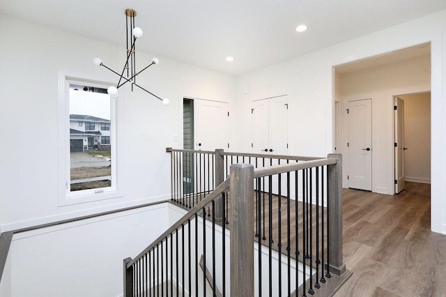 hall with baseboards, an upstairs landing, recessed lighting, an inviting chandelier, and wood finished floors