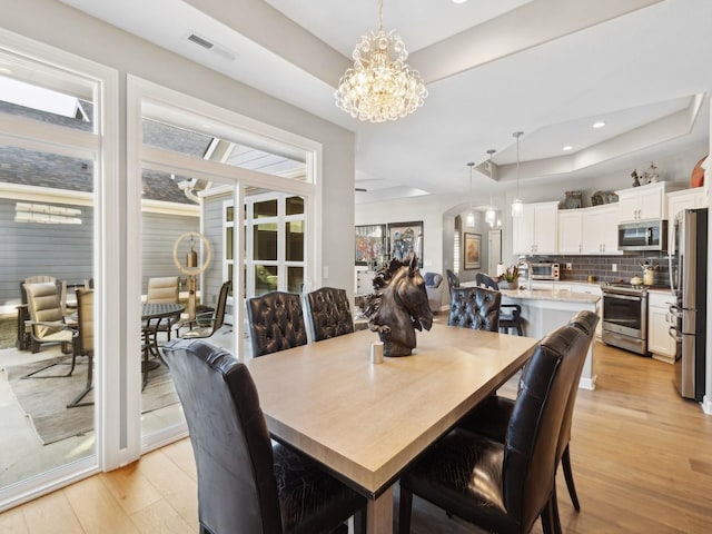 dining space featuring a raised ceiling, an inviting chandelier, and light hardwood / wood-style flooring