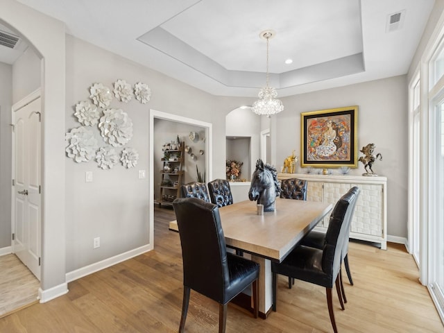 dining room featuring light wood-type flooring, a tray ceiling, and a notable chandelier