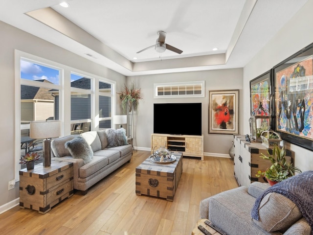 living room with light wood-type flooring, a raised ceiling, ceiling fan, and plenty of natural light