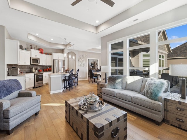 living room with light hardwood / wood-style floors, ceiling fan, and a raised ceiling