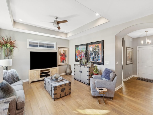 living room with ceiling fan, light wood-type flooring, and a raised ceiling