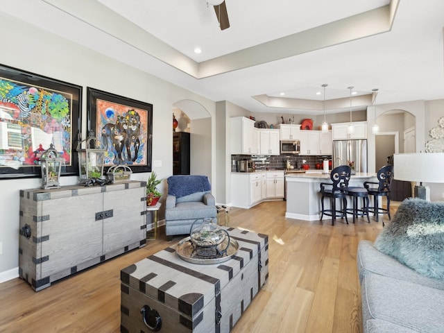 living room featuring ceiling fan, light hardwood / wood-style floors, and a tray ceiling