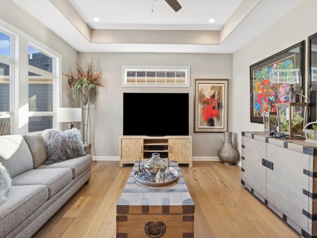 living room featuring ceiling fan, a tray ceiling, and light hardwood / wood-style flooring