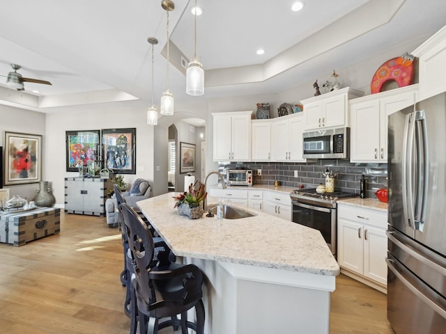 kitchen with hanging light fixtures, stainless steel appliances, a tray ceiling, white cabinets, and sink